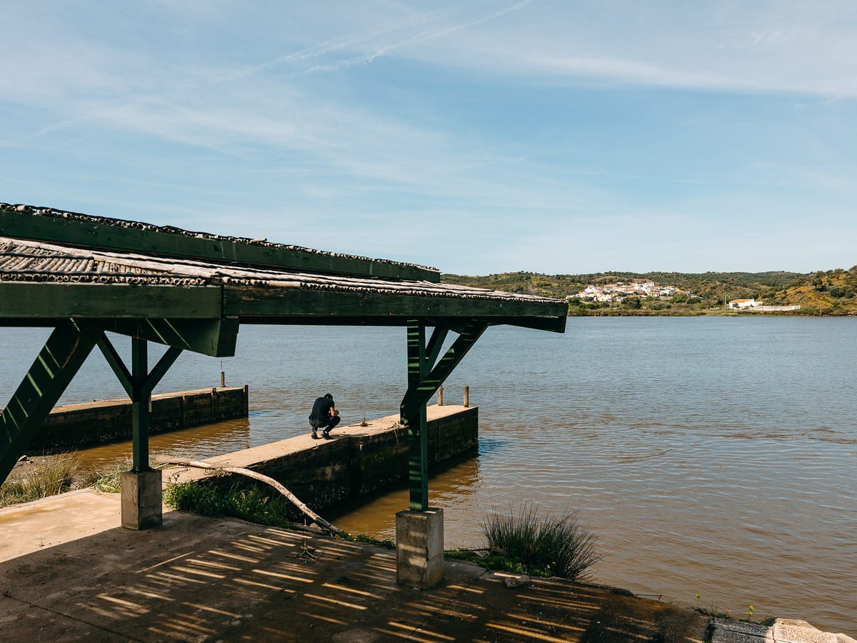 El embarcadero cubierto de la finca sobre el Guadiana, con la pasarela de madera y el caserío blanco de la orilla portuguesa al fondo