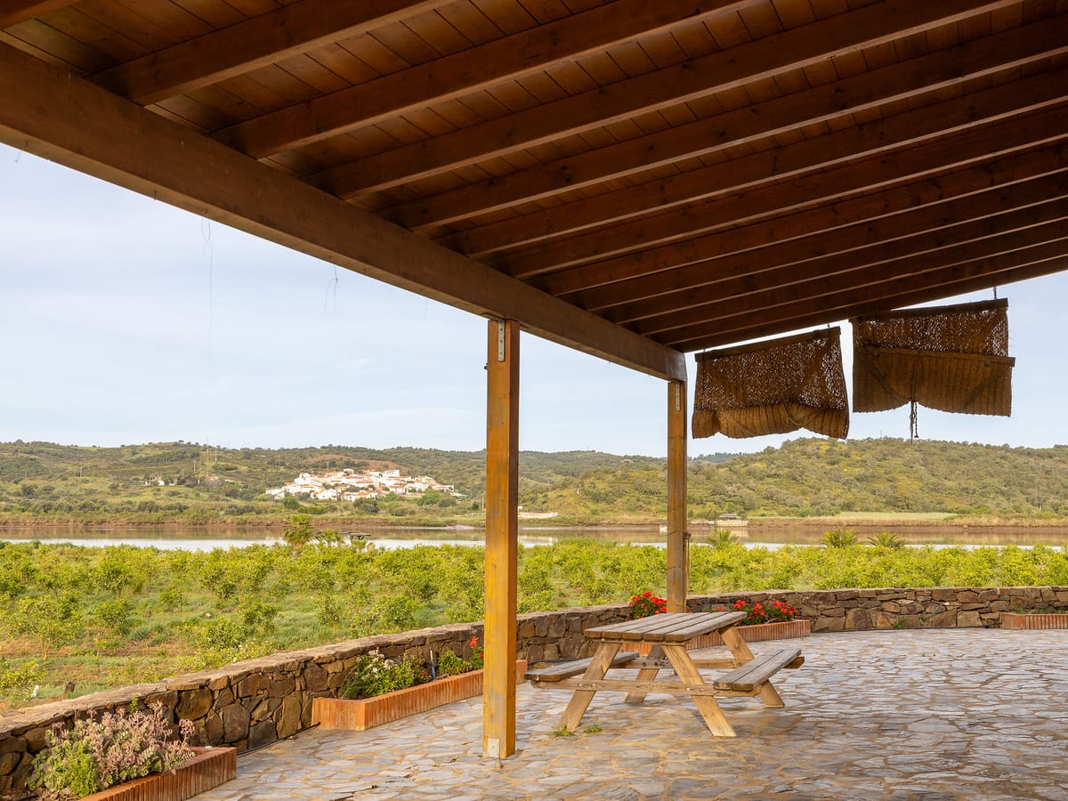 El porche del cortijo con la mesa de madera bajo la cubierta de cañizo, abierto a las plantaciones y al caserío blanco del fondo