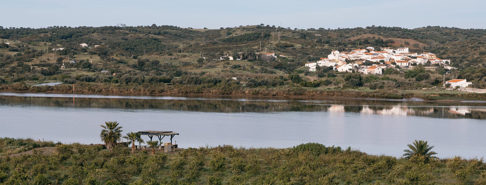 Las plantaciones bajando hacia el Guadiana, con el río en calma y un pueblo de casas blancas en la orilla portuguesa al fondo