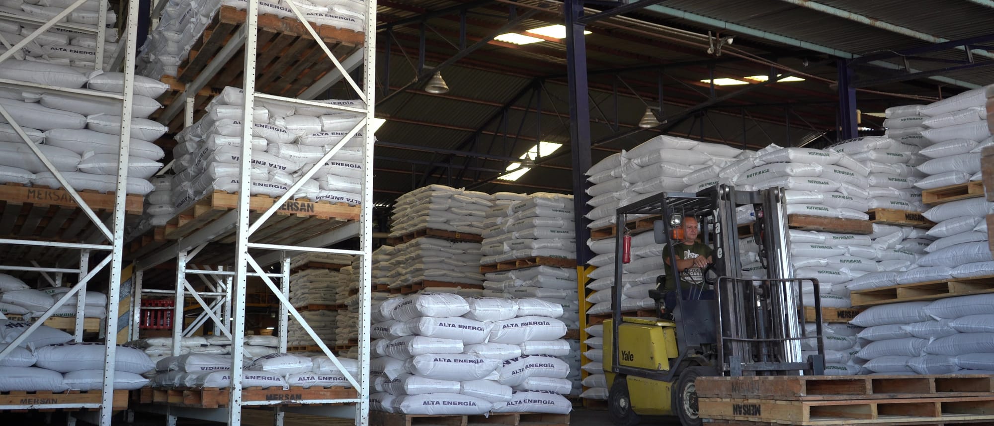 El almacén de la planta con las estanterías cargadas de sacos de alimento y un montacargas moviendo una paleta