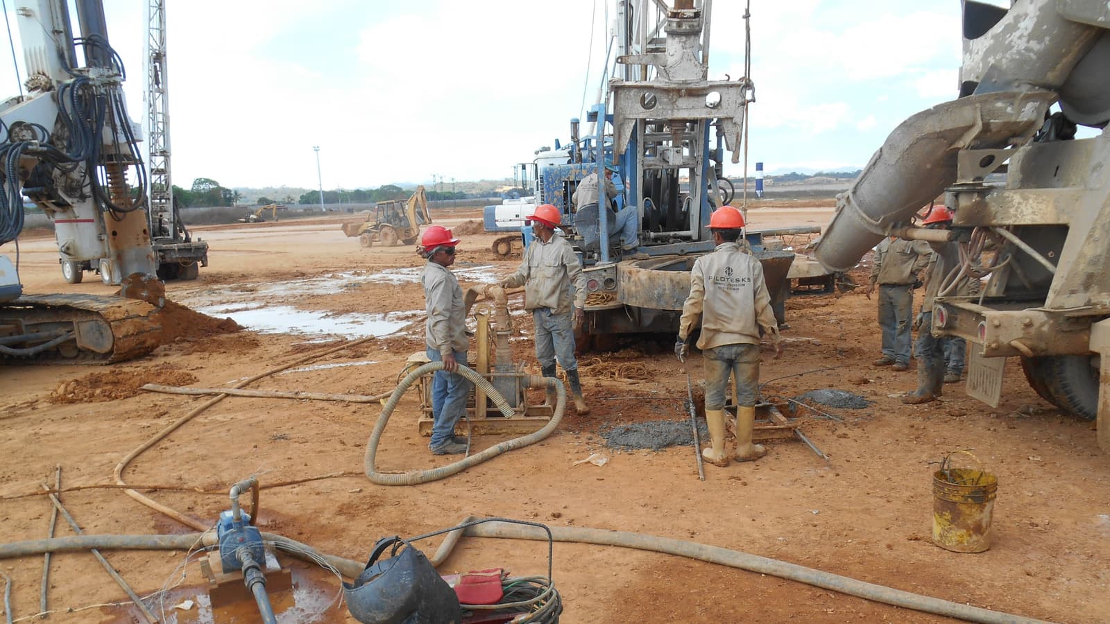 Cuadrilla de pilotaje con cascos rojos trabajando junto a las máquinas y el camión de concreto, en la plataforma de la planta de alimento balanceado