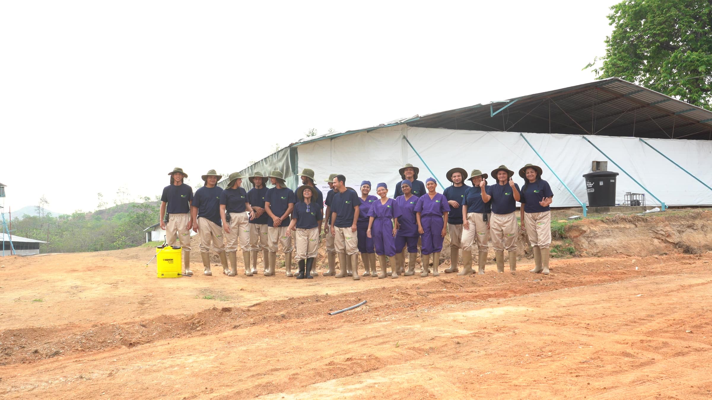 El equipo de la granja formado delante de uno de los galpones, con uniforme y botas de trabajo